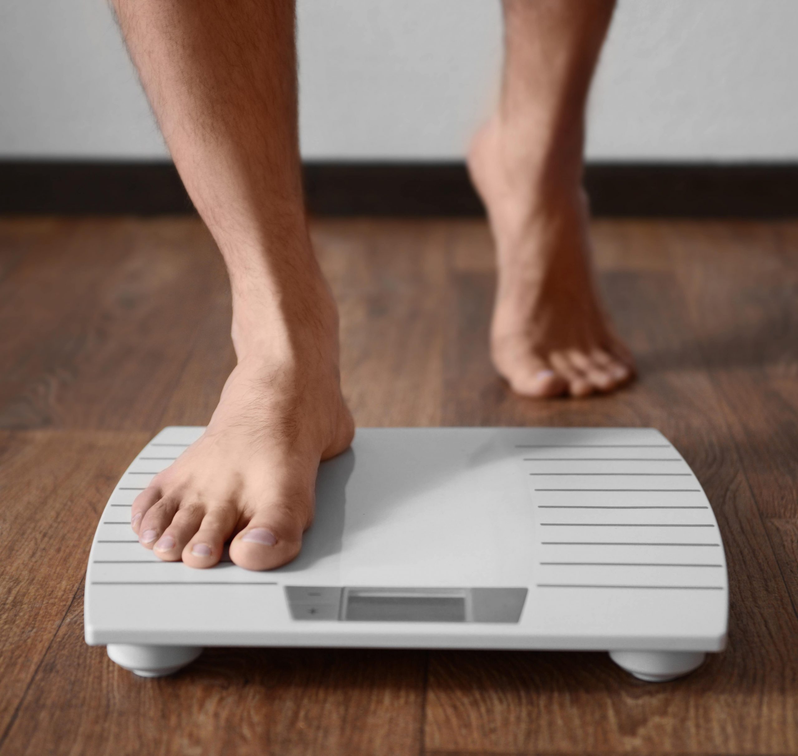Photo of a man stepping on a scale after natural weight loss