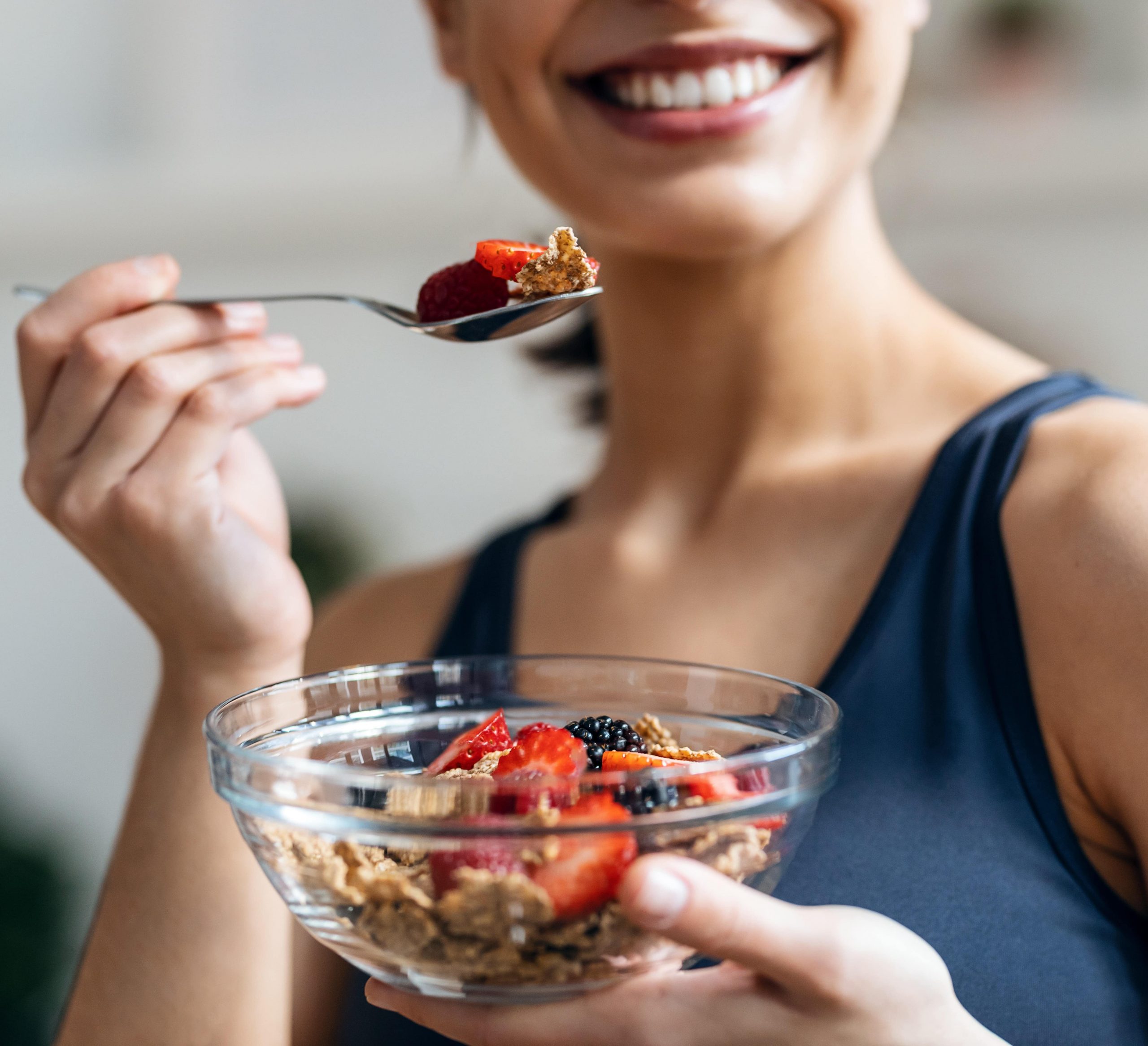 Athletic woman eating a healthy bowl of muesli with fruit in the kitchen at home