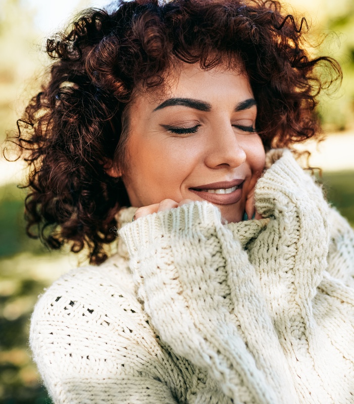 Outdoor close-up portrait of beautiful young woman smiling with closed eyes, posing against nature background with curly hair,