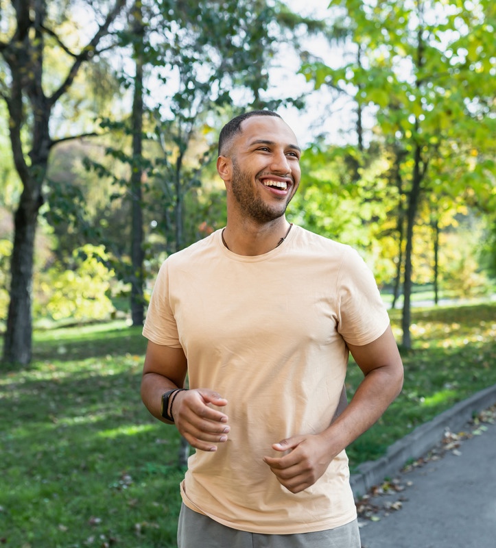 Cheerful man jogging in the park, man running on a sunny day, smiling and happy having an outdoor activity.