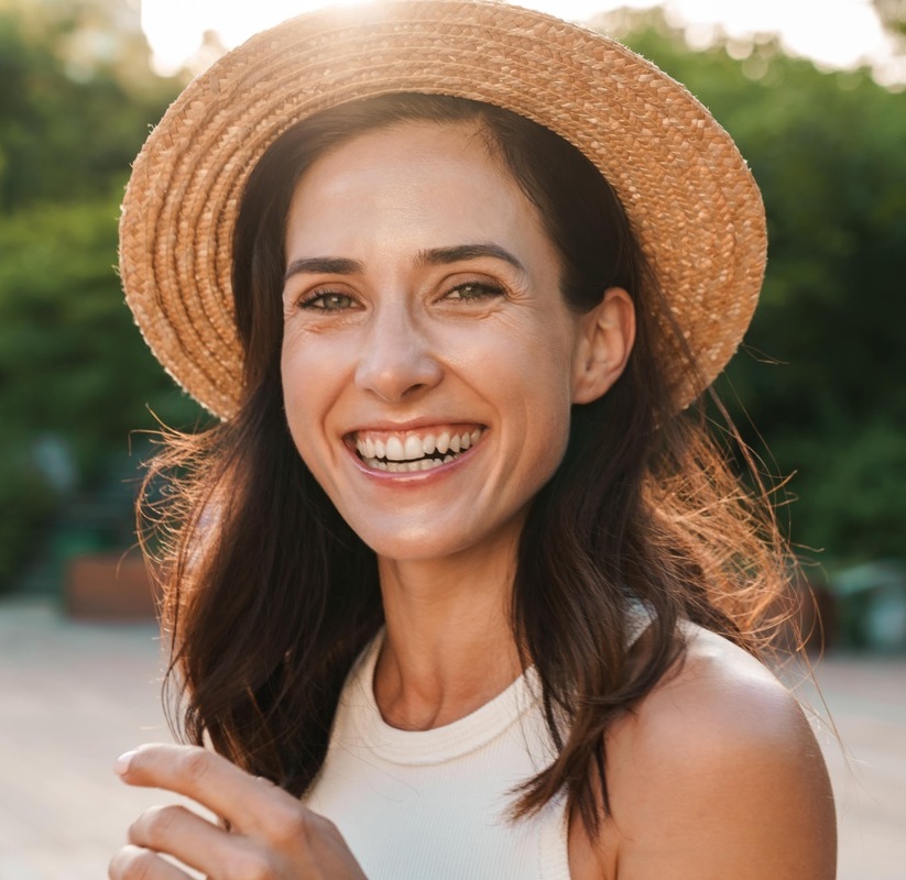 Image of beautiful middle-aged woman laughing and looking at camera while walking in summer park