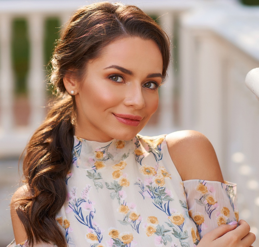 Pretty smiling young woman with long brunette hair wearing fashionable floral dress standing on street after lip enhancement treatments